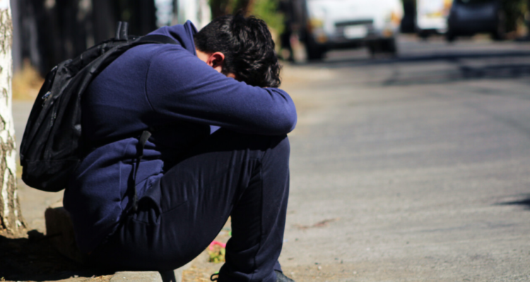 Estudiante sentado a la orilla de un camino, graficando un episodio de estrés escolar.