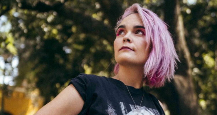 Camila Moreno posa con las manos en la cintura mientras mira hacia arriba. Se encuentra en un parque lleno de árboles. La artista fue uno de los ganadores de los Premios Pulsar 2022.