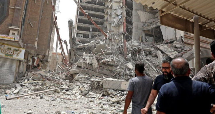 Varios hombre observan los escombros del edificio que se derrumbó en Abadan.