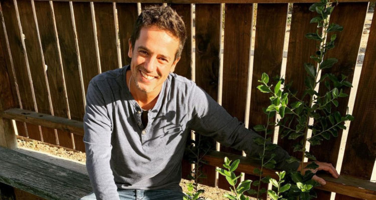 El actor Matías Oviedo sonríe a la cámara junto a una planta en su jardín.