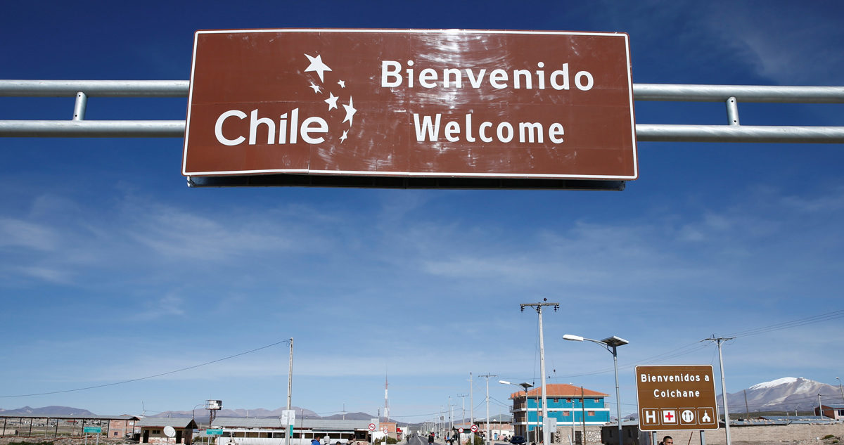 Migrantes caminan bajo un cartel que señala la entrada a Chile, el 13 de febrero de 2022, en los alrededores de la fronteriza comuna de Colchane (Chile), en una fotografía de archivo.
