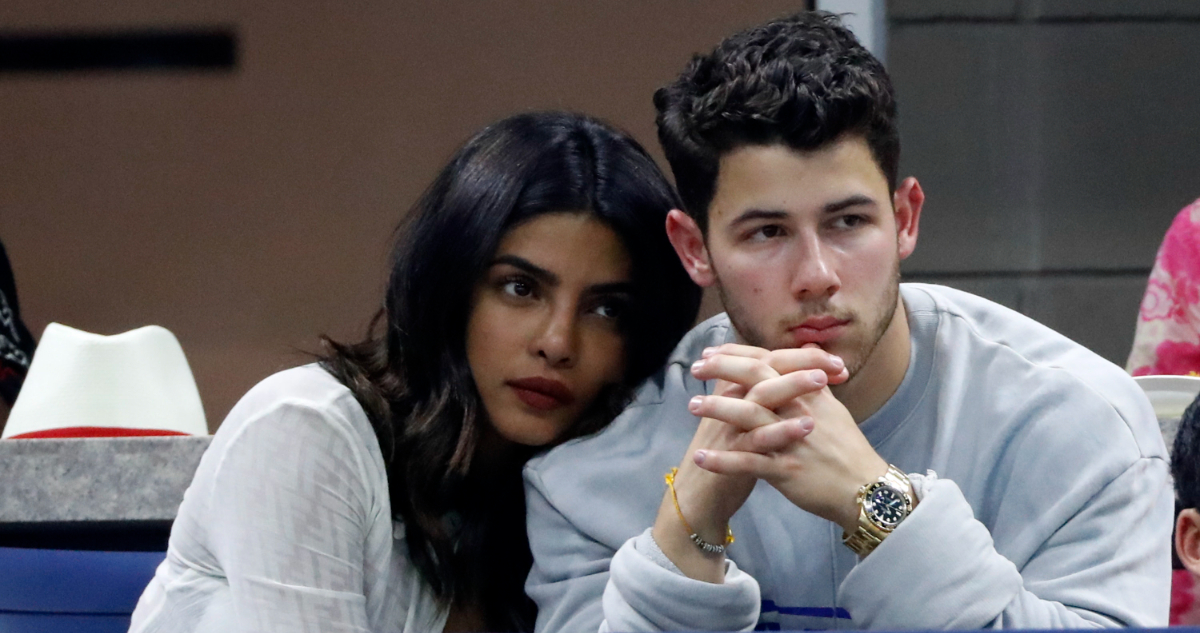 Nick Jonas y Priyanka Chopra abrazados serios mientras observan un partido de tenis.