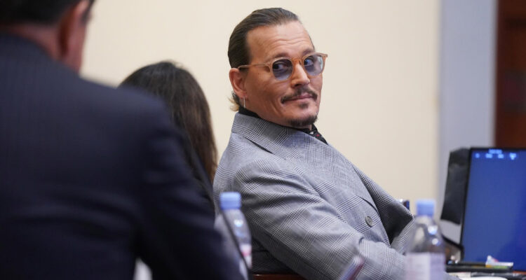Johnny Depp está levemente volteado con una media sonrisa mientras mira a sus abogados en medio del juicio en contra de su exesposa Amber Heard.