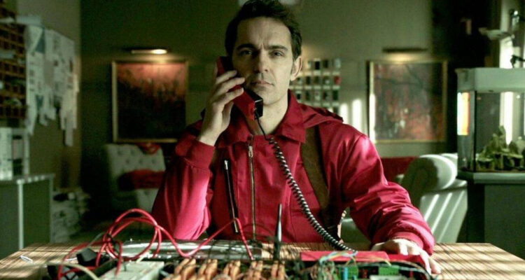 El actor Pedro Alonso interpretando a Berlín en La Casa de Papel. Aparece sosteniendo un teléfono mientras mira serio. El actor se encuentra en Chile para realizar una charla.