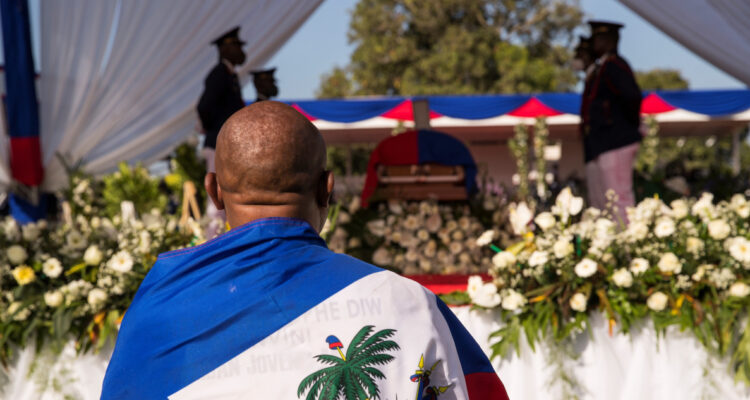 Un hombre envuelto con la bandera haitiana observa el féretro del presidente Jovenel Moise.