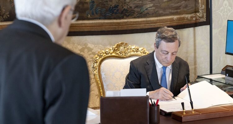 Mario Draghi firmando un documento ante el presidente italiano.
