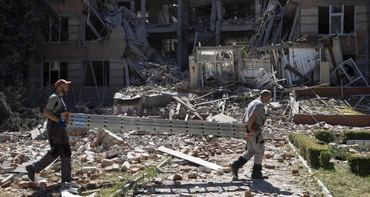 Dos hombres cargan una escalera frente a las ruinas del bachillerato técnico perteneciente a la Universidad de Economía Urbana, que resultó completamente destruido tras el ataque de artillería rusa.