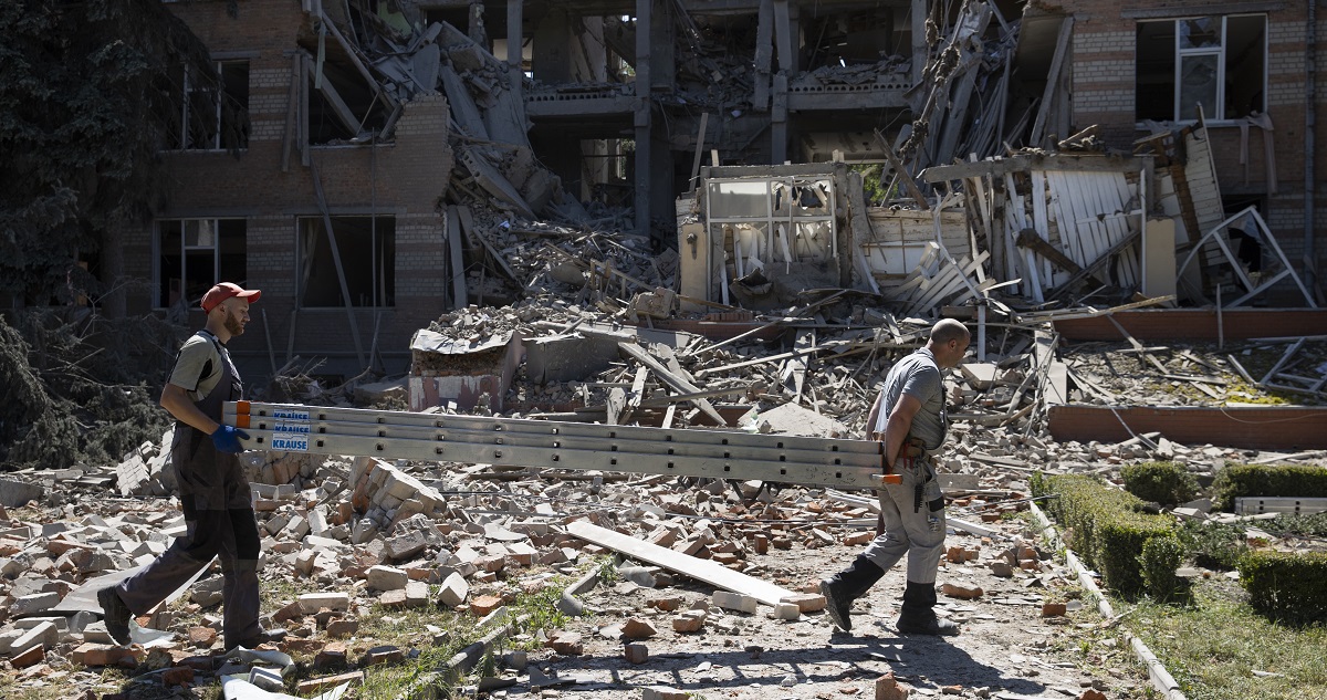Dos hombres cargan una escalera frente a las ruinas del bachillerato técnico perteneciente a la Universidad de Economía Urbana, que resultó completamente destruido tras el ataque de artillería rusa.