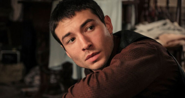 El actor Ezra Miller mira hacia atrás por sobre el hombro a la vez que está agachado.