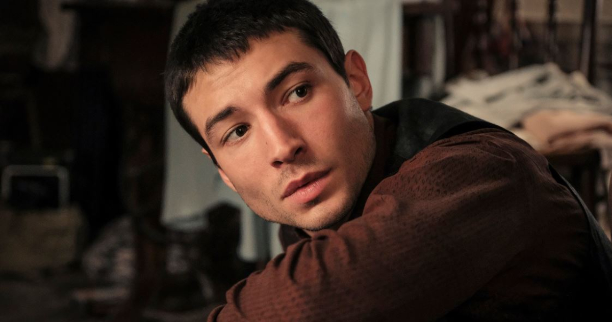 El actor Ezra Miller mira hacia atrás por sobre el hombro a la vez que está agachado.