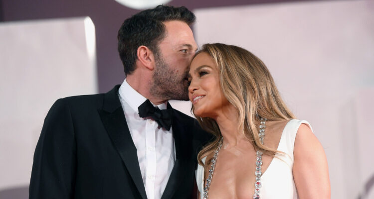 La cantante Jennifer López y Ben Affleck abrazados en un evento. El actor pareciera susurrar algo a su pareja mientras ella sonríe.