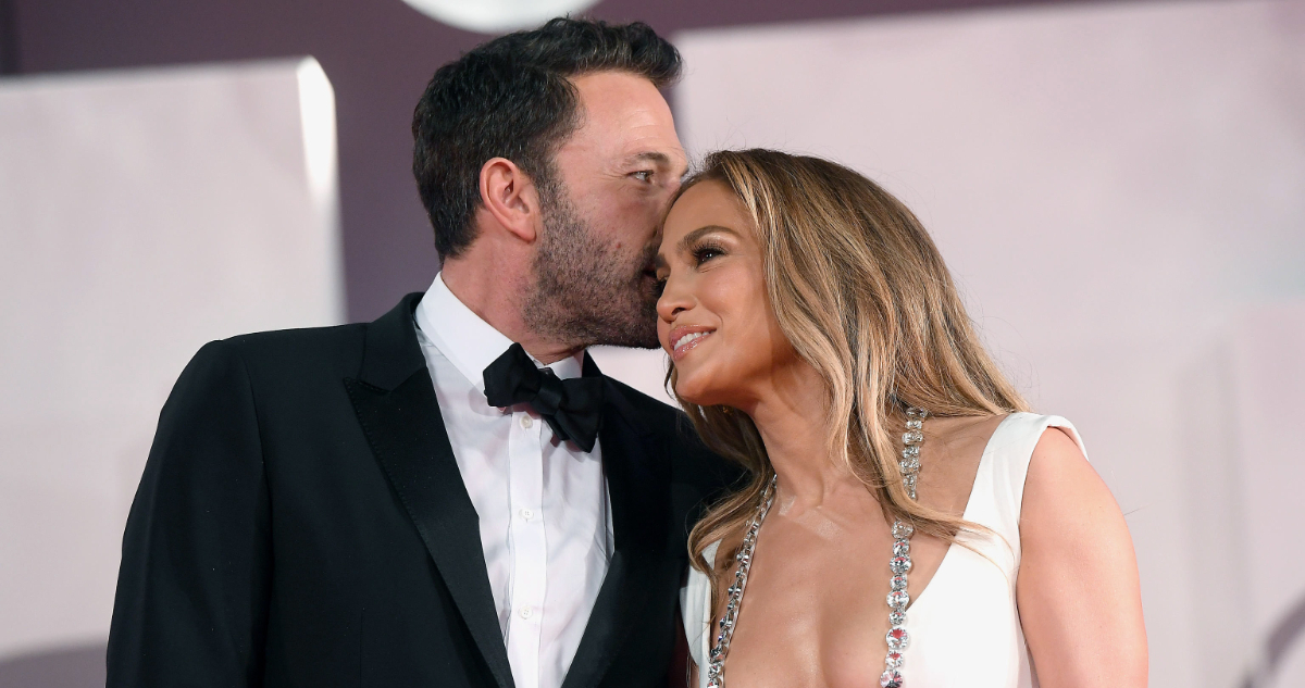 La cantante Jennifer López y Ben Affleck abrazados en un evento. El actor pareciera susurrar algo a su pareja mientras ella sonríe.