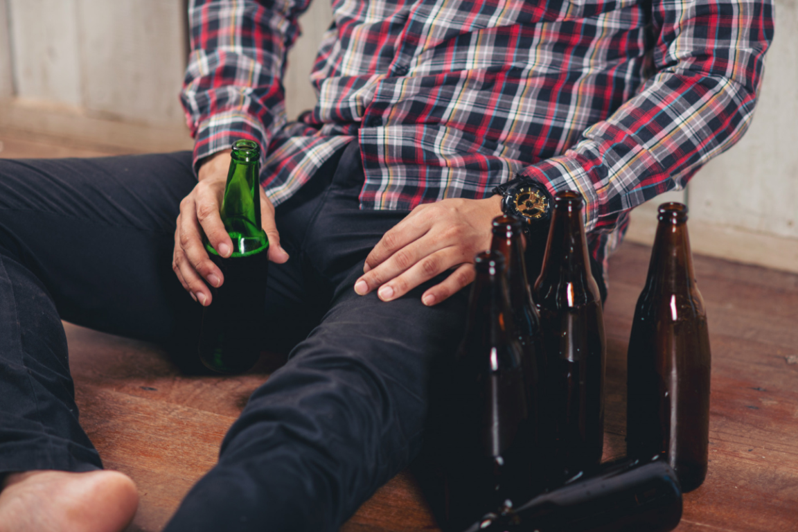 Persona con problemas de consumo de alcohol sentado en el piso con botellas de cerveza vacias