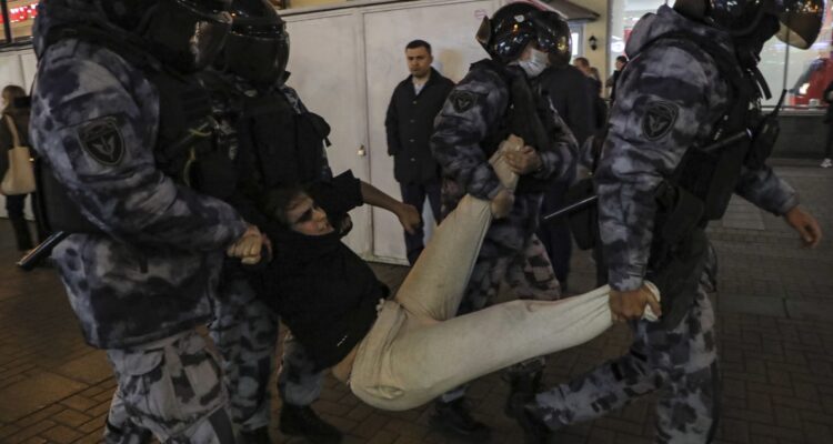 Cuatro policías rusos se llevan arrestado a un joven, sujetándolo de sus extremidades.