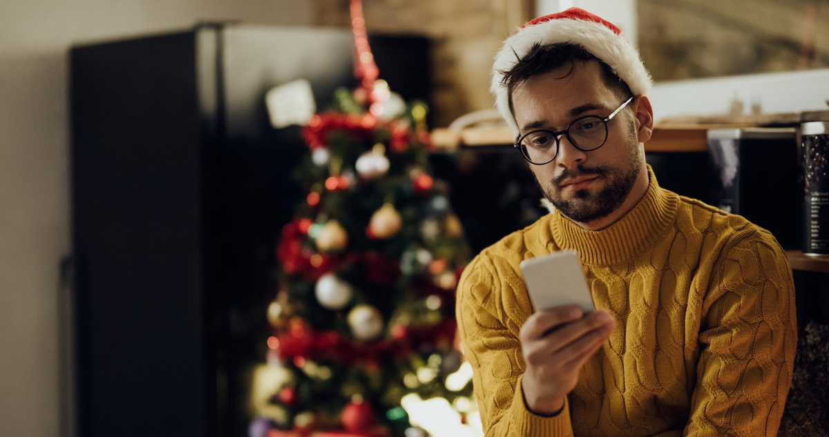 Hombre con sombrero de santa mirando su celular con expresión triste durante navidad. Depresión navideña