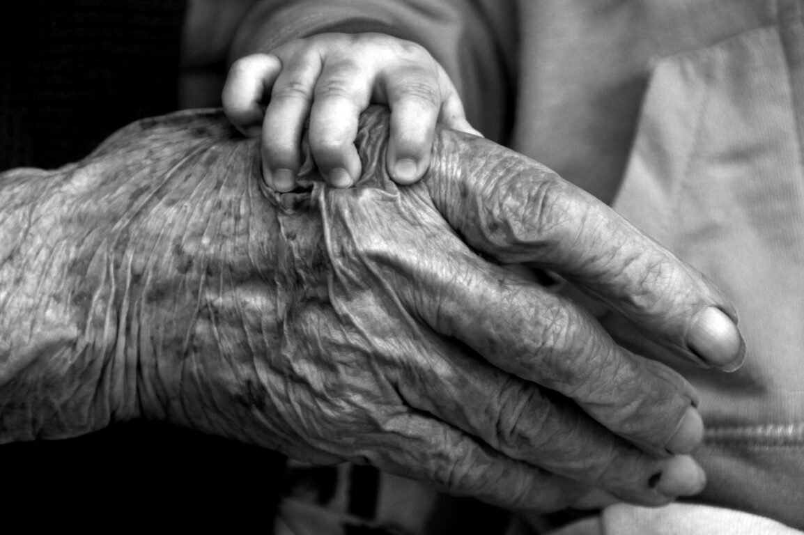 Fotografía en blanco y negro de mano de niño sobre mano anciana