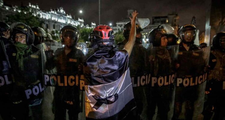 Un manifestante envuelto en una bandera de Perú con color negro en lugar del rojo, se para frente a policías, en una fotografía de archivo.