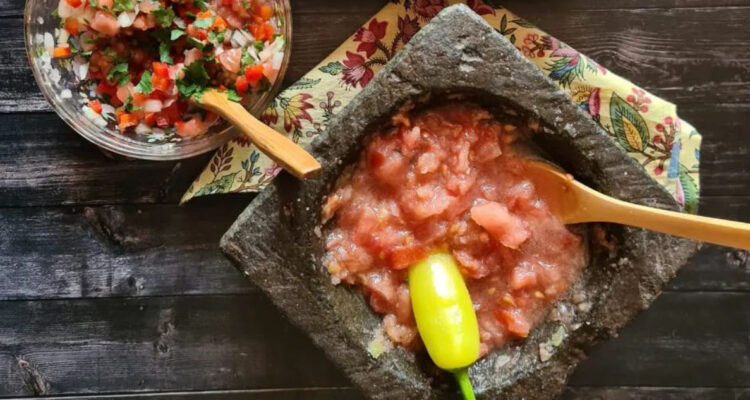 Un poco de salsa de Chancho en Piedra en una mesa junto a un plato con pebre. La salsa está en el ranking de los mejores platillos de América.