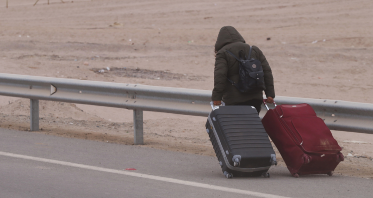 Persona caminando por la orilla de una carretera junto a dos maletas.