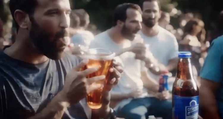 Captura del comercial creado con inteligencia artificial en que personas que no existen disfrutan de una cerveza ficticia.