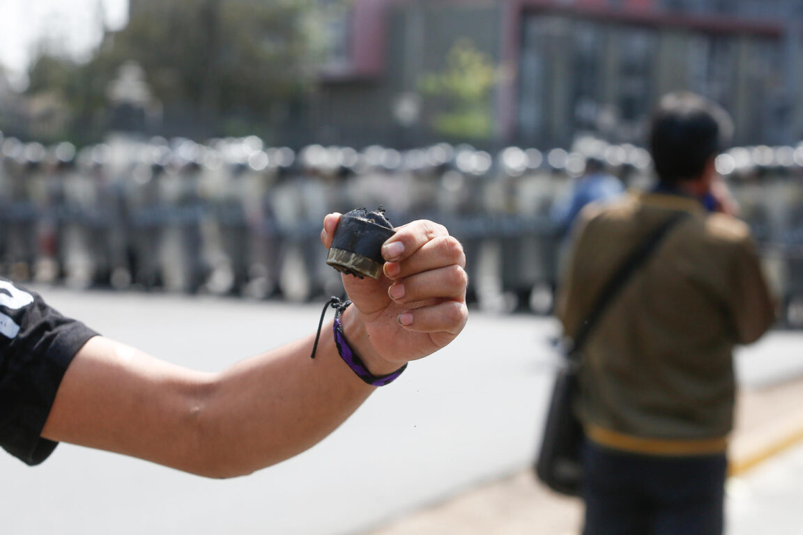 Un manifestante muestra un casquillo mientras manifestantes chocan con policías en Lima