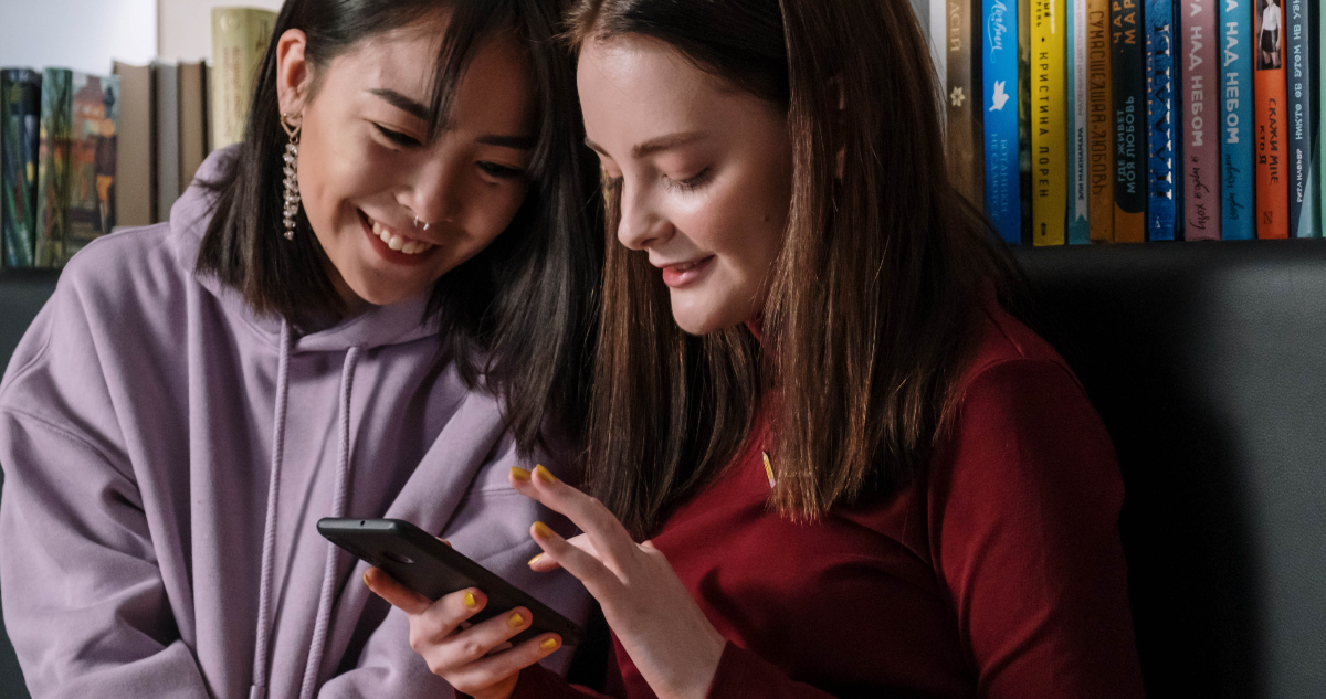 Dos chicas ríen mientras miran un celular. China realizó un plan para poder restringir el uso de celulares en menores de 18.