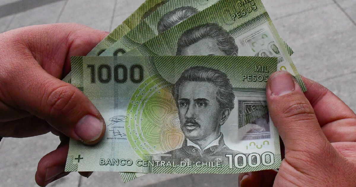 Billetes de mil pesos sostenidos por los dedos de un hombre