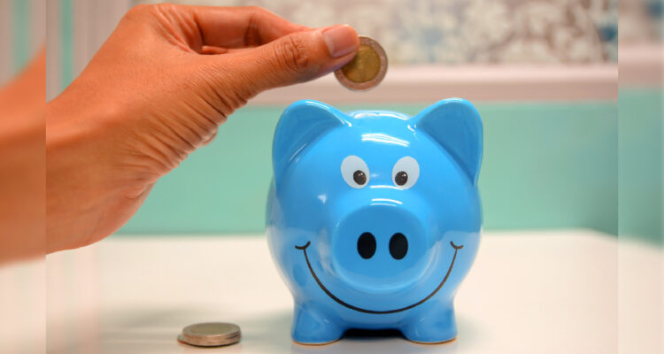 una mano dejando una moneda en una alcancía de chanchito