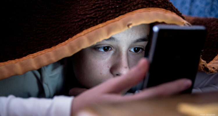 Niño oculto entre las sábanas usando su celular