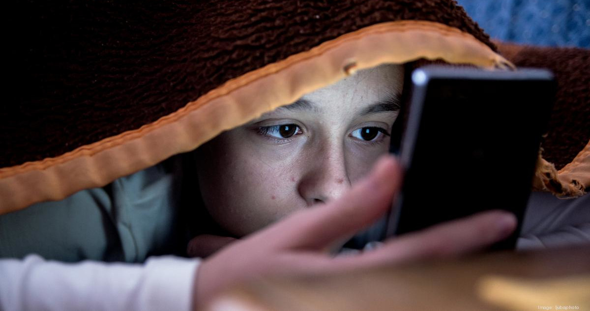 Niño oculto entre las sábanas usando su celular