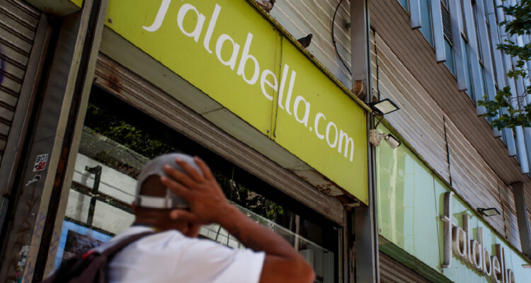 Frontis de una tienda falabella, y en el fondo a la izquierda un hombre observa los logos de la compañía