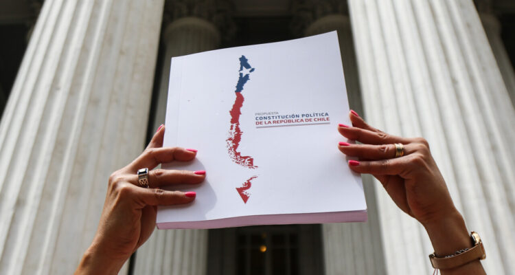 Una mujer levanta el libro de propuesta de nueva constitución frente a la sede del ex Congreso, donde se discutió la propuesta del Consejo Constitucional.