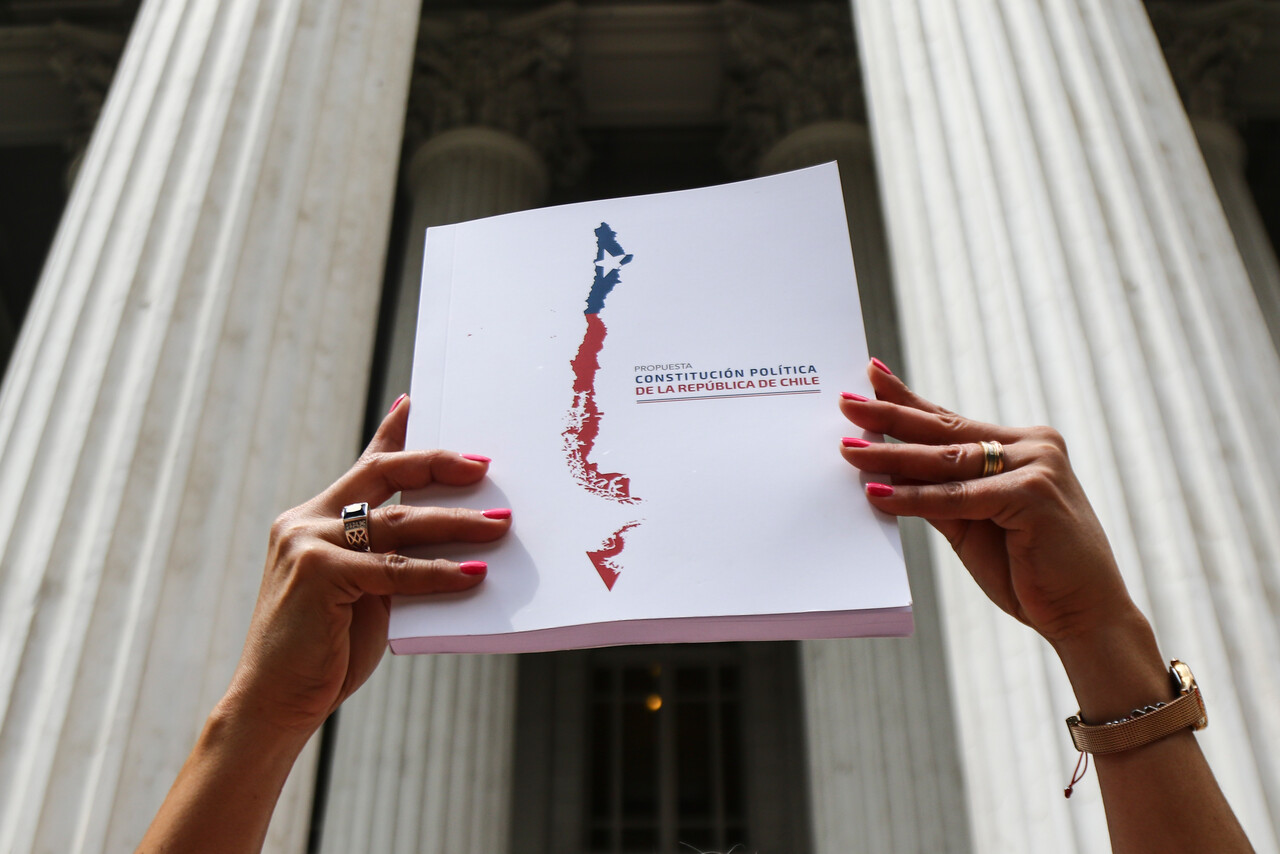 Una mujer levanta el libro de propuesta de nueva constitución frente a la sede del ex Congreso, donde se discutió la propuesta del Consejo Constitucional.
