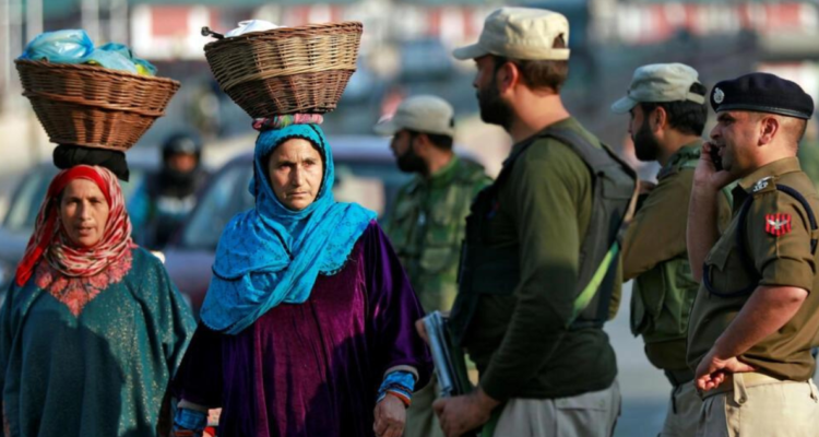 Mujeres de Cachemira caminan junto a policías indios en una calle de Srinagar en octubre de 2019