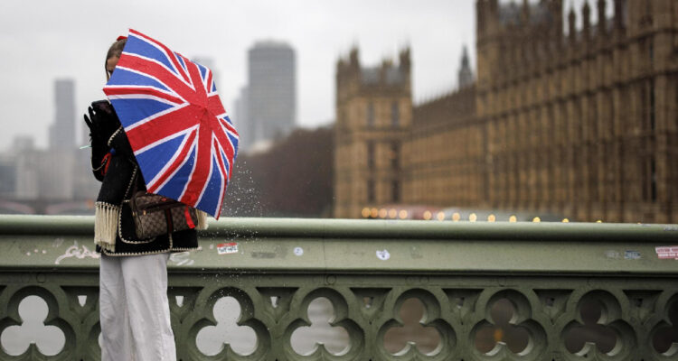 Una persona con un paraguas pintada con la Union Jack en un día de lluvia. Detrás: el palacio de Westminster