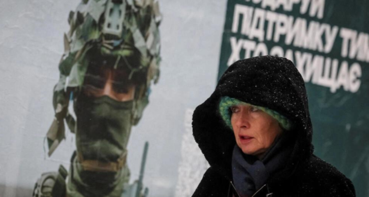 Una mujer junto a un cartel de un militar ucraniano durante una nevada en Kiev