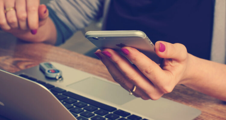 mujer sosteniendo un iphone y navegando por internet en un notebook