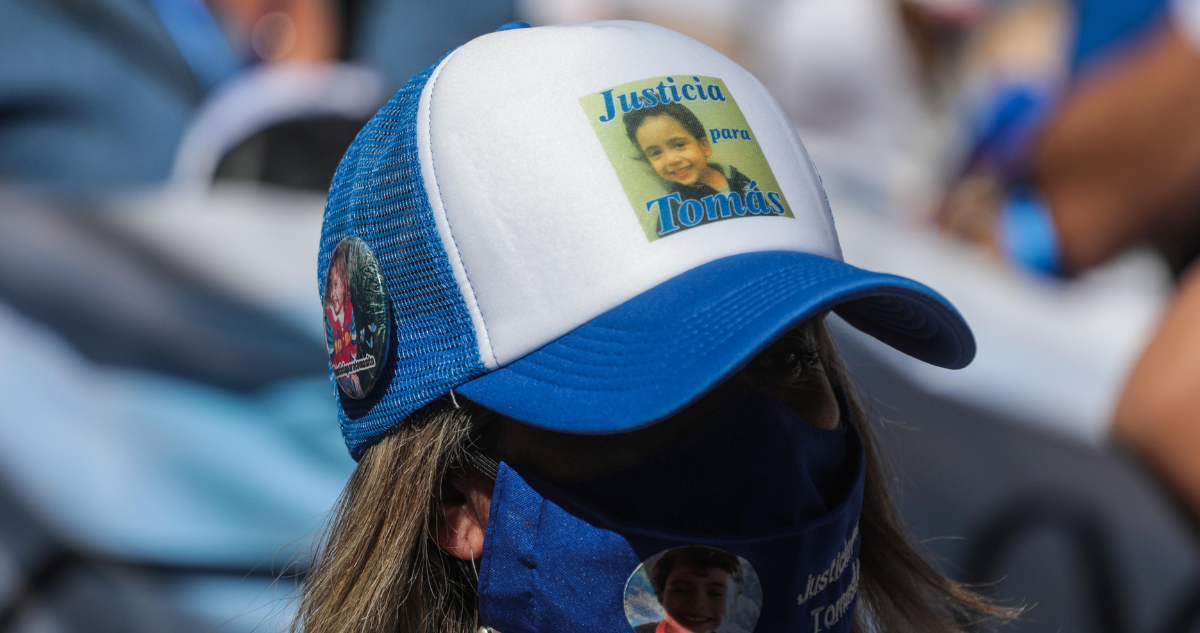 Mujer usando gorra con foto de Tomás Bravo por aplazamiento de preparación de juicio
