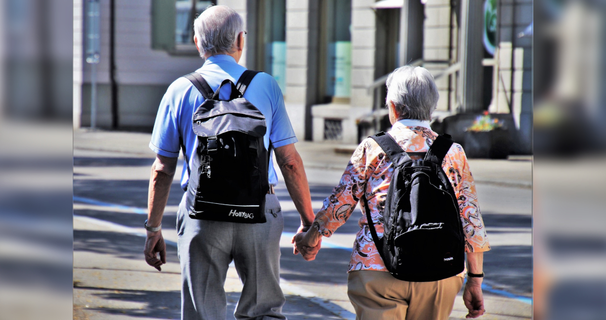 una pareja de adultos mayores con mochilas en sus espaldas y tomados de la mano