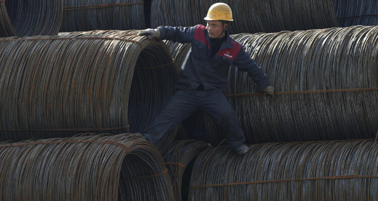 Un trabajador chino escala entre diversos rollos de alambre de acero