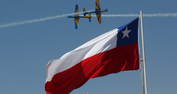 Bandera de Chile ondeando mientras de fondo dos aviones realizan acrobacias en la fidae 2022