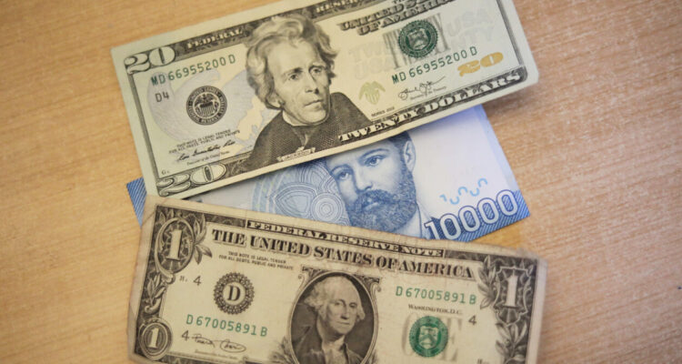 dos billetes de dólares en primer plano, escondiendo un billete de diez mil pesos