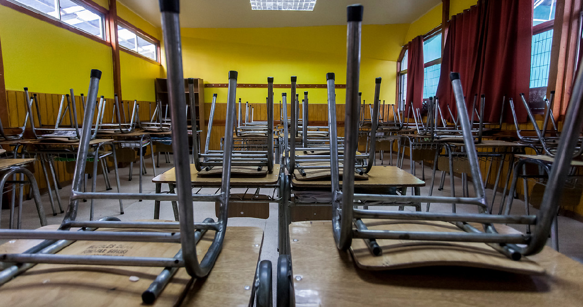 imagen de una sala de clases vacías y con sillas arriba de las mesas