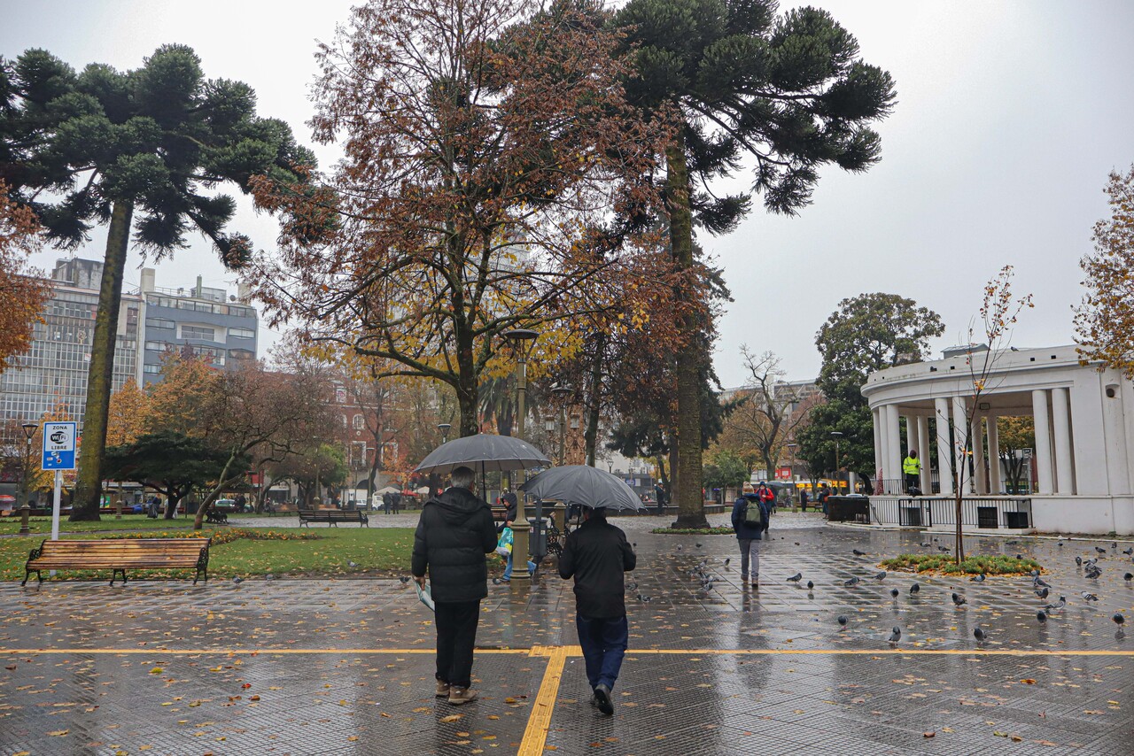 Transeuntes circulan por la plaza de la ciudad, en una nueva jornada de lluvias en la Region del Biobio