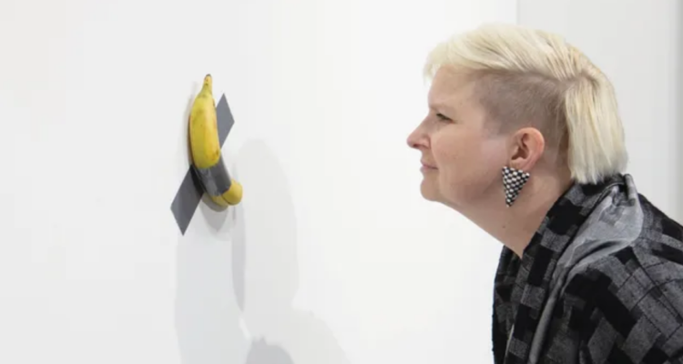 Persona contemplando obra de arte Comedian, o más conocida como el plátano pegado a la pared con cinta adhesiva