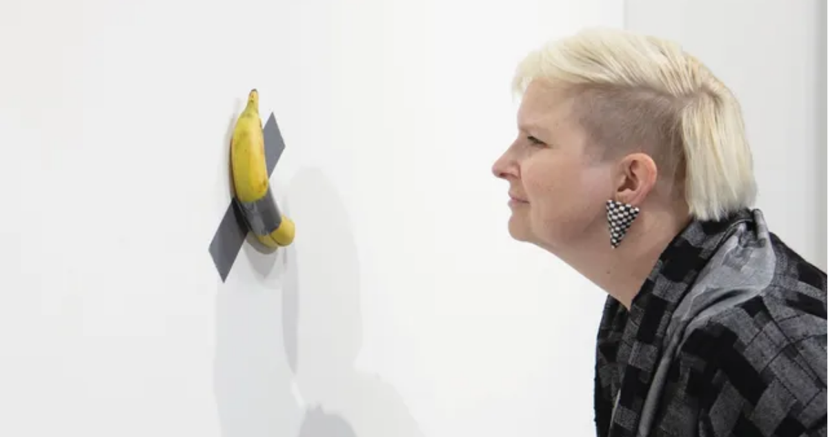 Persona contemplando obra de arte Comedian, o más conocida como el plátano pegado a la pared con cinta adhesiva