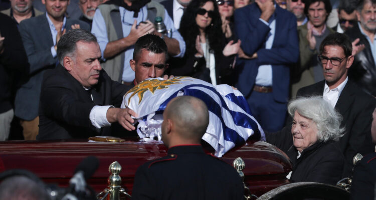El presidente de Uruguay, Yamandú Orsi (i) extiende una bandera sobre el ataúd del exmandatario José Mujica, junto a Lucía Topolansky (d)