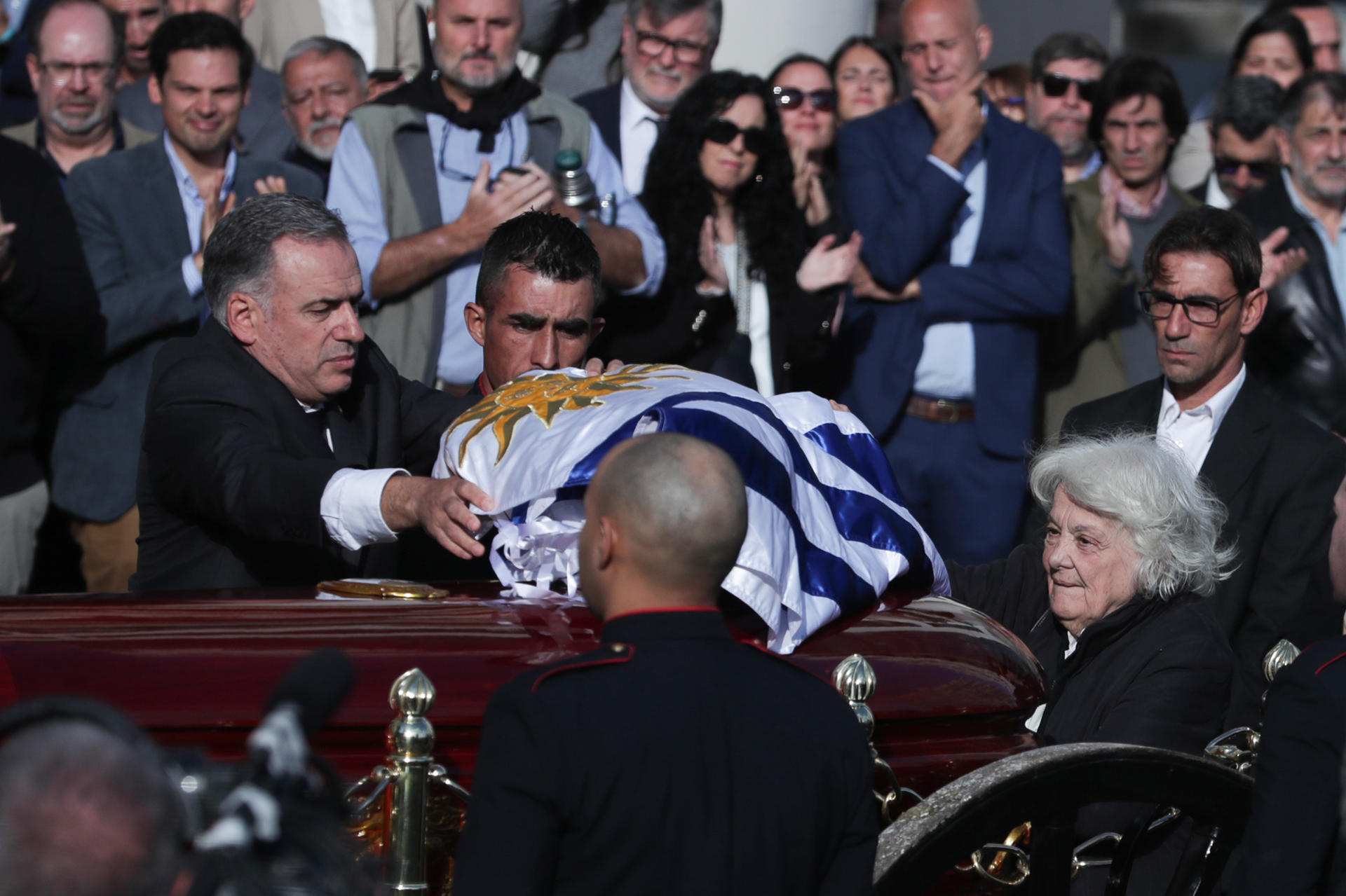 El presidente de Uruguay, Yamandú Orsi (i) extiende una bandera sobre el ataúd del exmandatario José Mujica, junto a Lucía Topolansky (d)