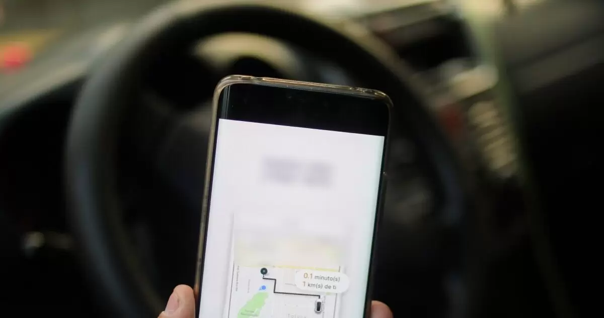 Teléfono con pantalla de aplicación y volante de automóvil detrás.
