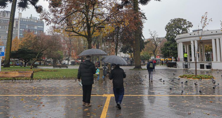 Se ve dos personas con paraguas, de espaldas, plaza de la Independencia de Concepción.